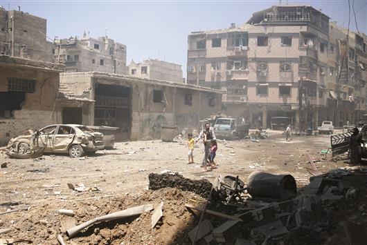 سوري مع اطفاله يمرون وسط الدمار في بلدة دوما في ريف دمشق امس (رويترز)