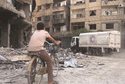 فتى سوري يمر بدراجته في حي في حرستا في ريف دمشق يقوم فيه الهلال الاحمر السوري بتوزيع مساعدات أمس (أ ف ب)