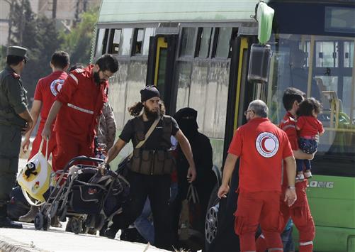 عناصر من "الهلال الأحمر السوري" يساعدون على نقل المسلحين وعائلاتهم إلى حافلات عند حاجز للجيش على اطراف حي الوعر في حمص امس (أ ف ب)
