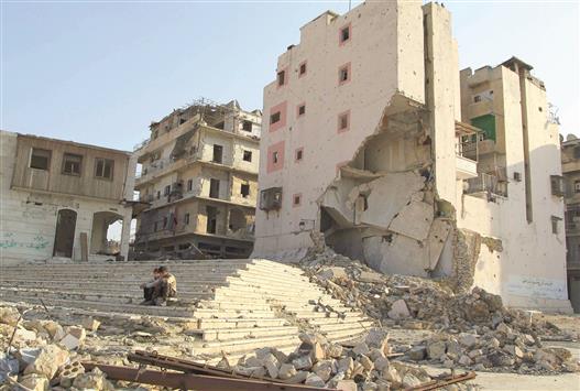 سوريان يجلسان قرب مبنى مدمر في حلب امس (رويترز)