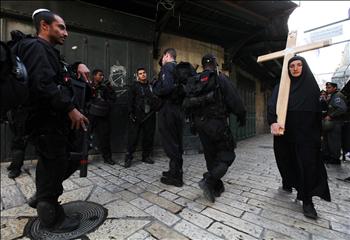 امرأة تحمل صليباً على طريق الآلام أمام عناصر من شرطة الاحتلال الإسرائيلية في القدس المحتلة أمس.