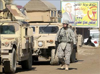 جندي للاحتلال أمام ملصق انتخابي في كربلاء أمس