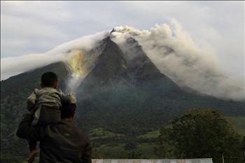 رجل يحمل ابنه على كتفه، يراقب بركان سومطرة وهو ينفث الرماد والدخان في مقاطعة كارو، شمالي الجزيرة.