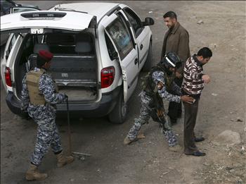 شرطيان عراقيان يفتشان رجلاً عند حاجز في بغداد أمس