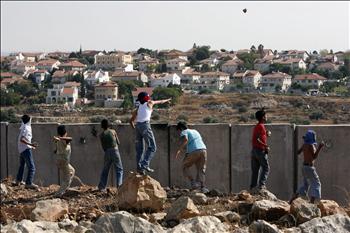 فلسطينيون يرشقون الحجارة من فوق جدار الفصل أمام مستوطنة في نعلين أمس.
